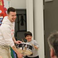 Child learning to play the snare drum posing for a picture with an instructor at a Bandology community band workshop