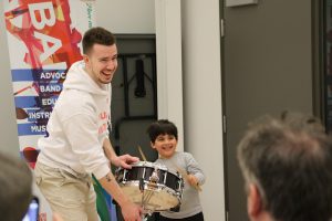 Child learning to play the snare drum posing for a picture with an instructor at a Bandology community band workshop