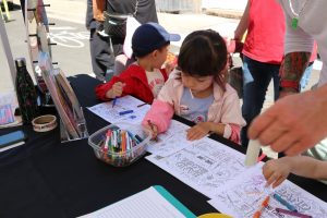 Kids coloring music-themed worksheets at an outdoor family activity table in a Bandology community event